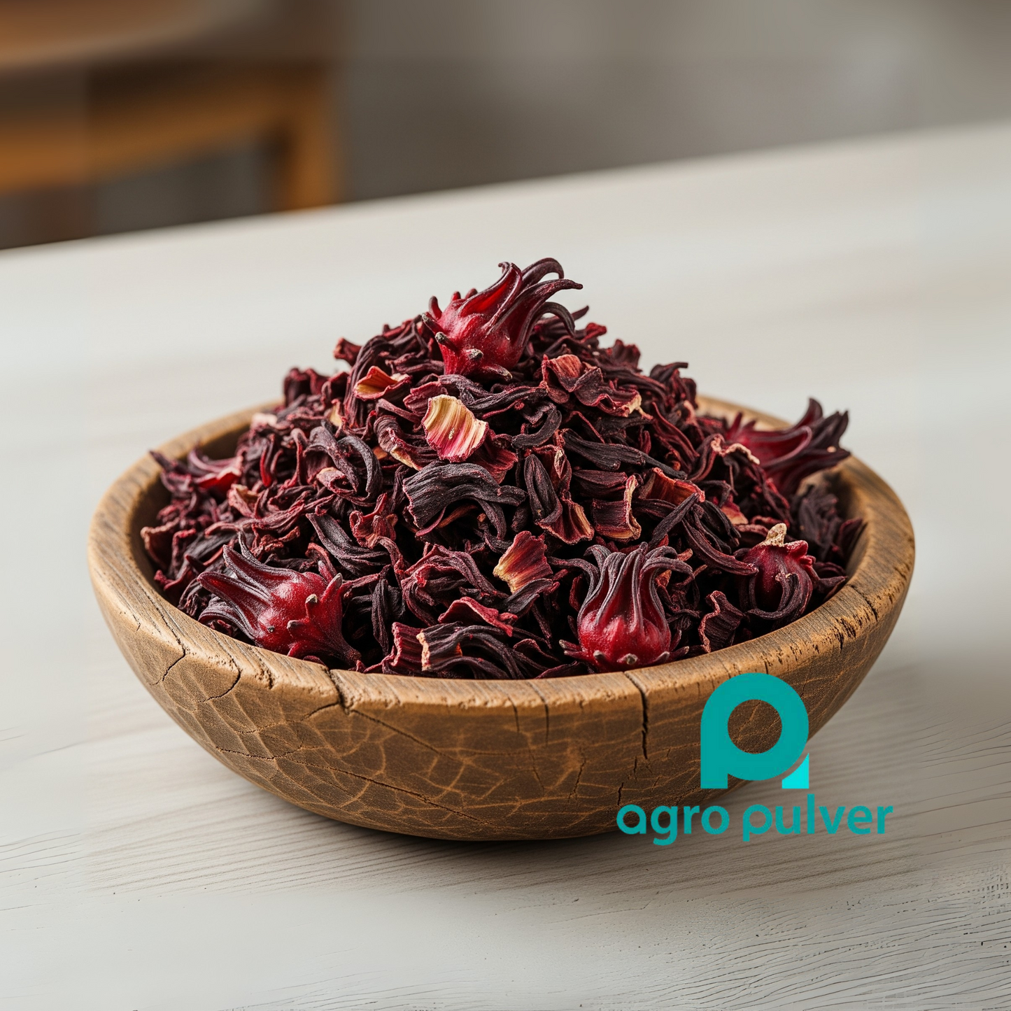 Wooden bowl filled with dried red hibiscus flowers on a light surface, featuring the Agro Pulver logo.